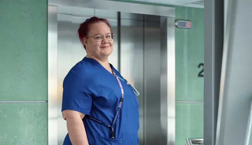 Sairaanhoitaja Virve Köppä hoitajan asussa. Seisoo hissien edessä.