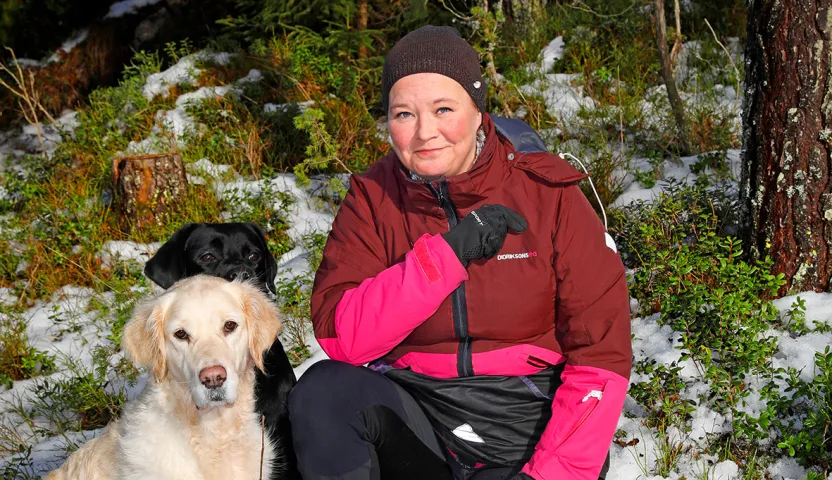 Tia Majanen kyykyssä koirien kanssa metsässä.