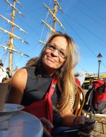 Sirpa Podrouzekin kasvokuva. Taustalla iso purjevene.