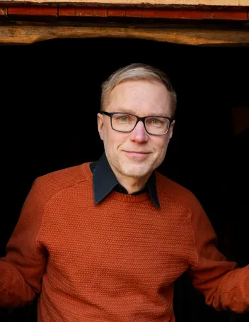 Mauno Kinnusen kasvokuva, päällään poltetun oranssin värinen villapaita.