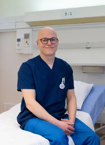 Sairaahoitaja Mikko Ståhle istuu potilasvuoteella ja katsoo hymyillen kameranaan.
