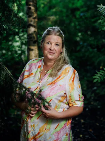 Eini Elomaa kuvattuna ulkona puiden katveessa.