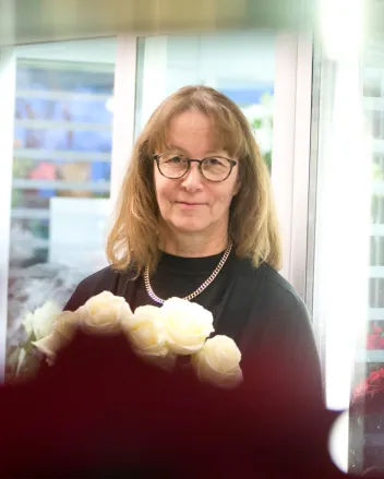 Kukkakaupan pitäjä Riitta Karjula kädessään kimppu valkoisia ruusuja.